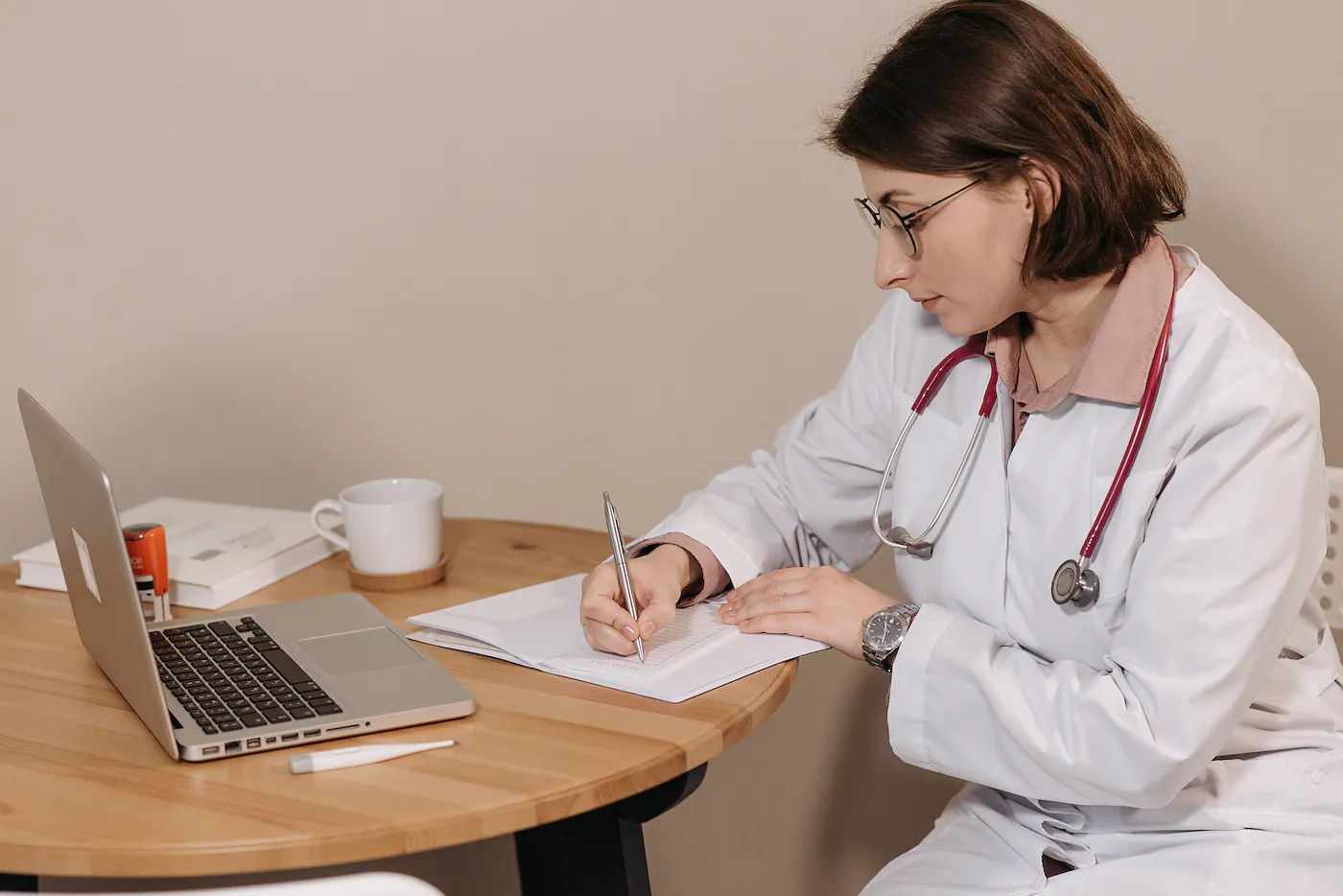 Médica con bata y estetoscopio revisando notas de un paciente en su consultorio