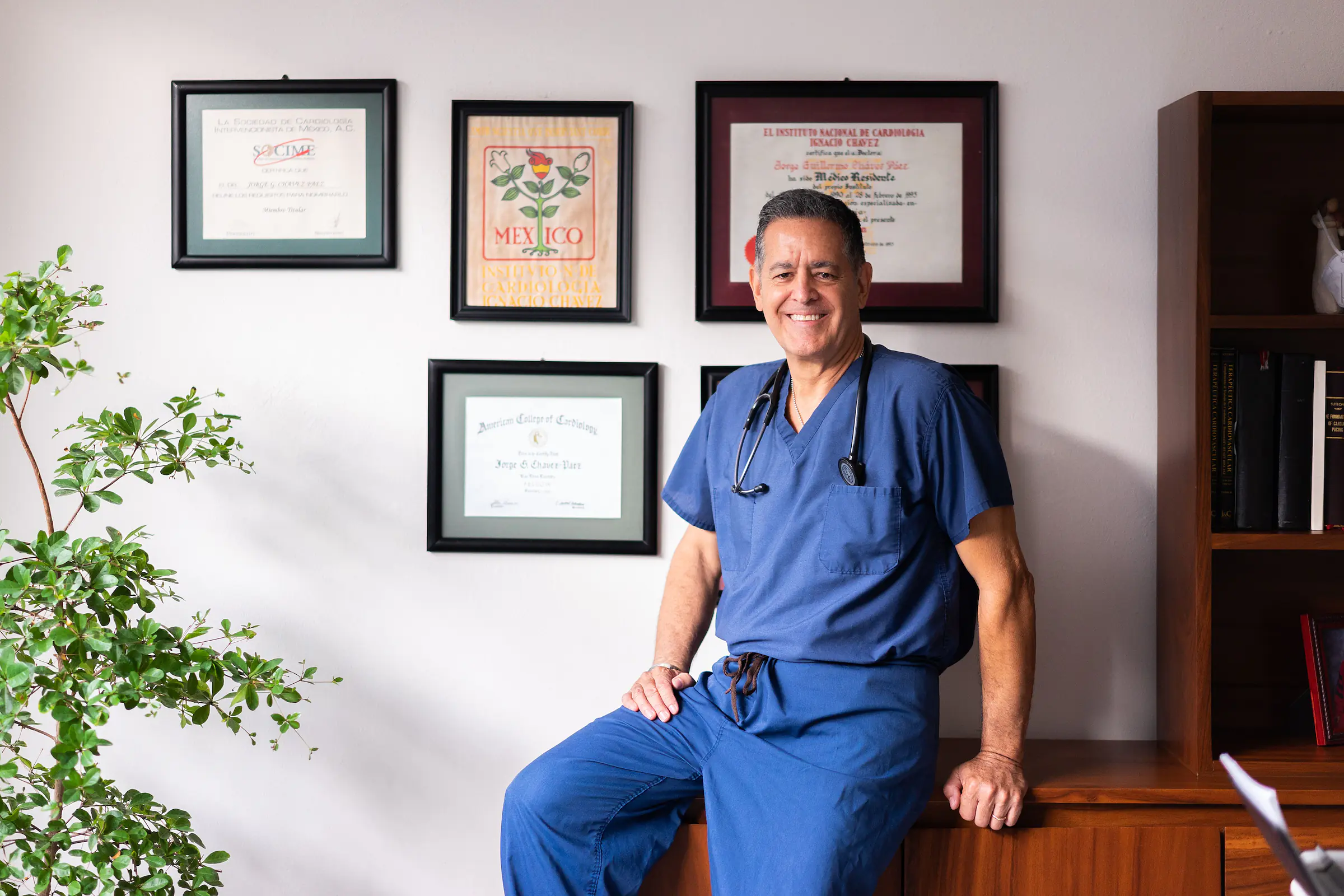 Médico con estetoscopio sonriendo en su consultorio, frente a sus certificados de cardiología